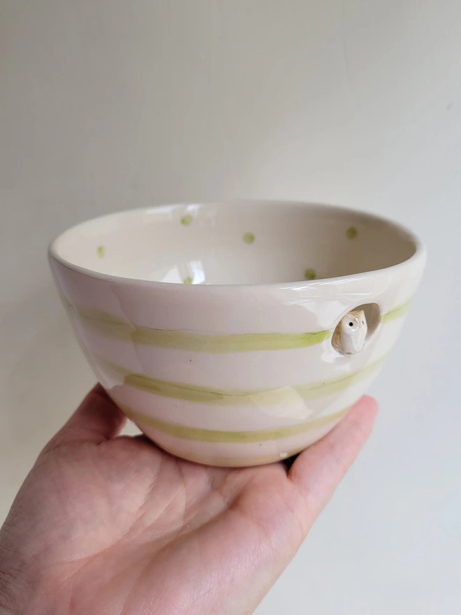 pottery owl bowl held in a hand with ceramic modelled owl inside a circular cut out green stripes to the outside and green dotty pattern inside