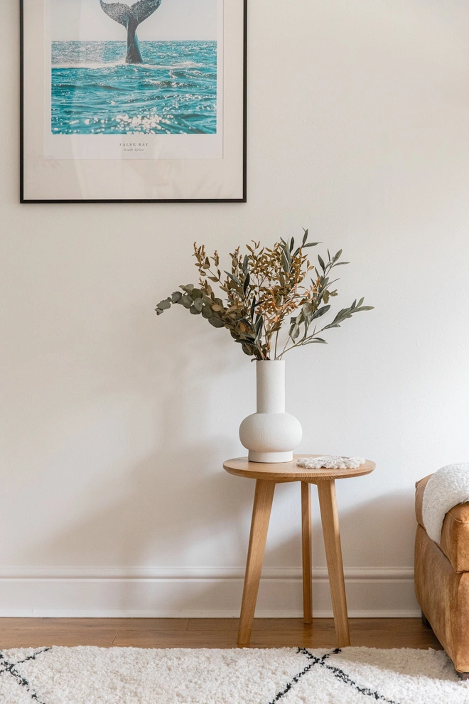 Handmade Solid Oak Side Table, a wooden side table sitting on a carpet in a living room. It is accompanied by a vase and a picture. 