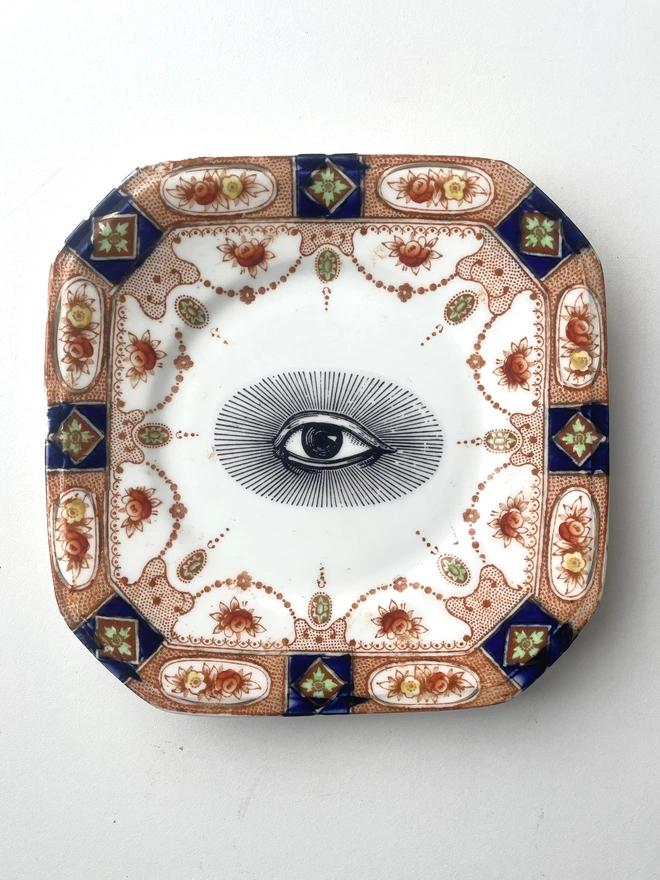 an ornate vintage plate with detailed patterned border, in the centre is printed an eye