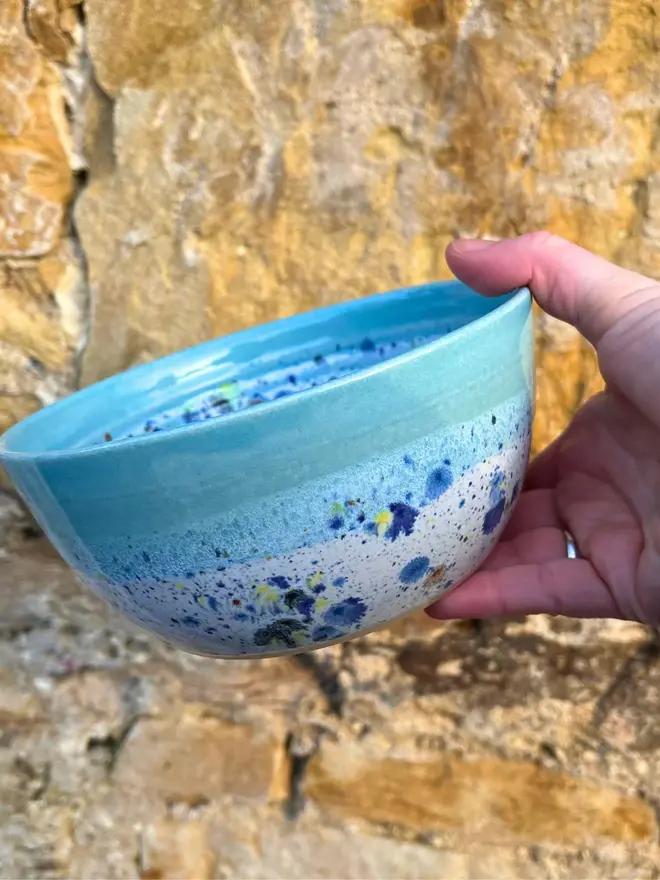 Shoreline Small Bowl, a colourful bowl held in front of a brick wall. 