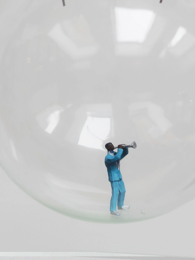 Miniature figure of a jazz musician playing a trumpet in a glass Christmas bauble - close up 
