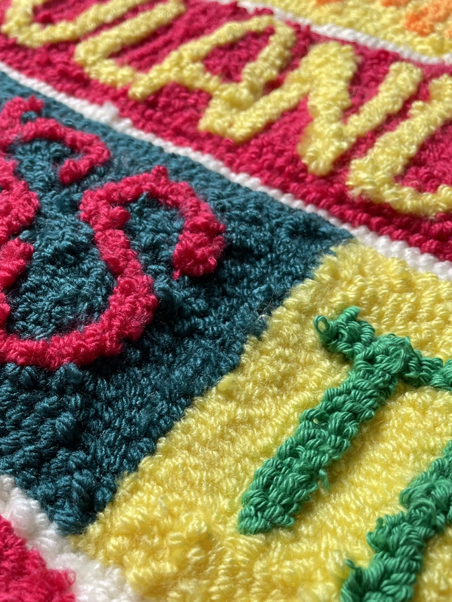 punch needle wool type in bright coloured wool on contrasting square background