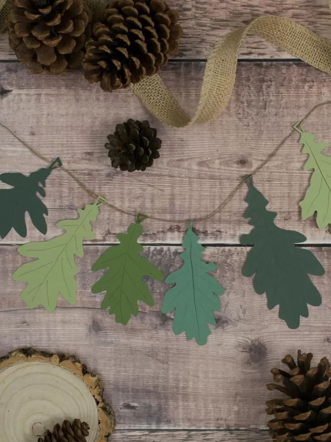 Green Oak Leaf Garland laying on a wooden board. Leaf colours shown include sage, dark green, olive green and apple green.