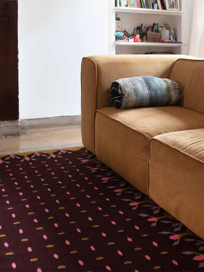 Hedgerow Flatweave Rug, a colourful rug sitting in a decorated room. It is accompanied by some household items.