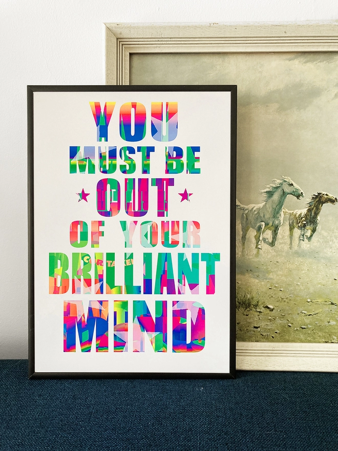 Framed multicoloured typographic poster with song lyric by the band, Furniture - "You must be out of your brilliant mind”.  The print rests against a 1960's print of galloping horses.