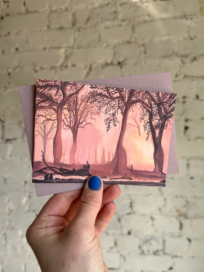 a greetings card featuring an illustration of a landscape of a sunset coming through trees with a few silhouettes of baboons enjoying it too with a muted purple envelope