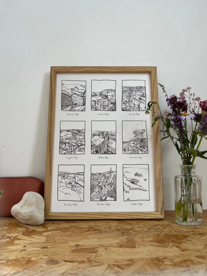 a print featuring an fine line illustration of nine edges of the peak district in a frame next to some flowers and a rock