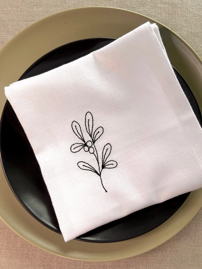 White cotton embroidered Christmas mistletoe napkin, styled on green and black place setting