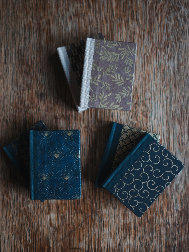 Three sets of miniature books in assorted prints in brown and gold, navy and gold, and black and gold