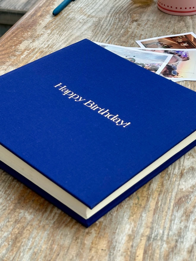 a side view of a navy blue linen photo album which has been printed with the words Happy Birthday on the front.