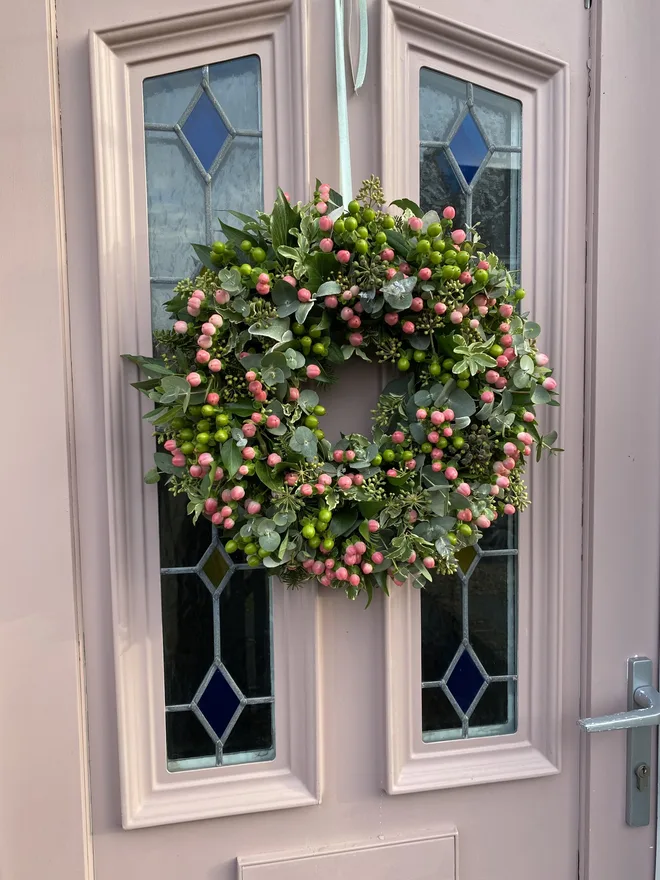 Floral hypericum door wreath. a green floral wreath featuring leaves and buds hung on a beige door.