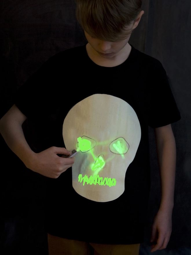 Boy drawing with torch onto glow tshirt with skull print