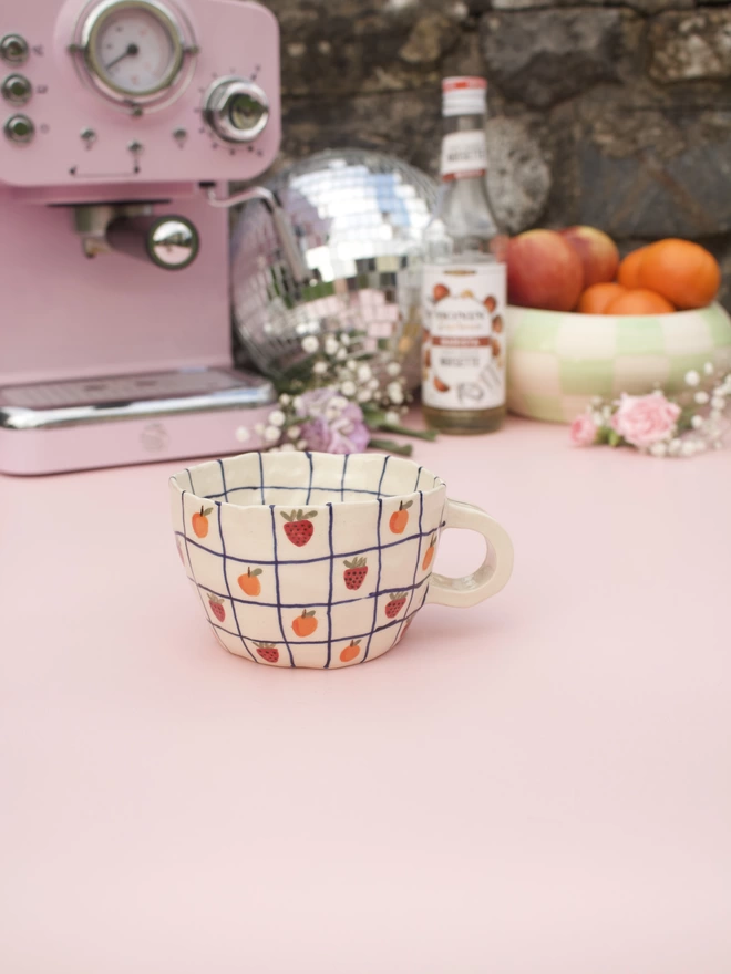 handmade stoneware pottery mug with a blue grid design and handpainted strawberries and oranges