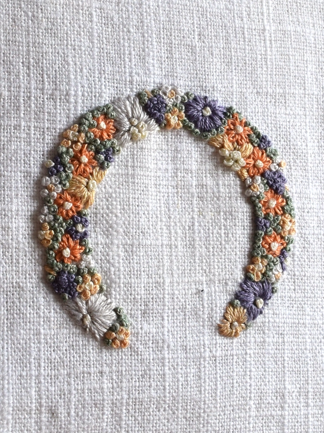 An embroidered Sunshine Garden Horseshoe of Golden Yellows and Bright Orange Blossoms with Green French Knot grass background.  