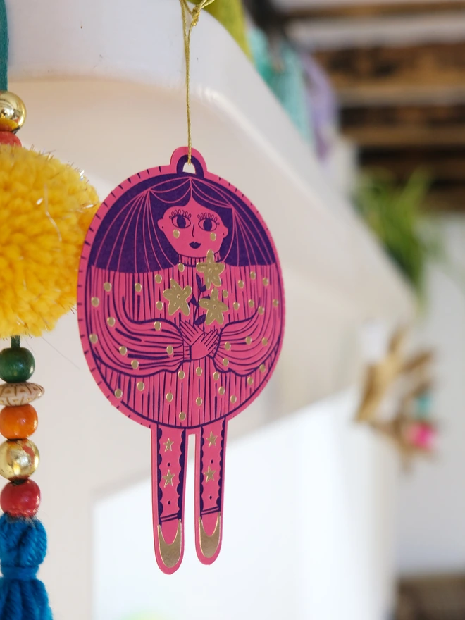 Christmas bauble lady printed blue and gold on pink card. Hanging with gold string. 