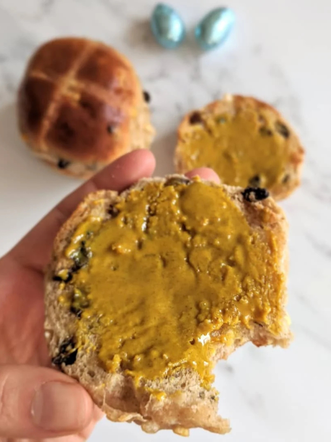 maple turmeric cashew butter. a half-eaten hot cross bun spread with maple turmeric cashew butter.