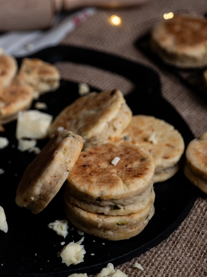 La Mexicana Savoury Welsh Cakes on a black bakestone griddle with scattered broken cheese 