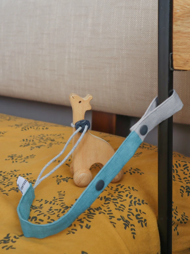 Handmade blue linen toy strap with grey string and a toggle attached to wooden baby toys,