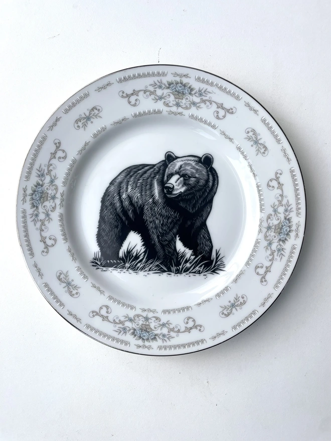 a vintage plate with an ornate border, in the centre of the plate is a vintage style black and white illustration of a big bear