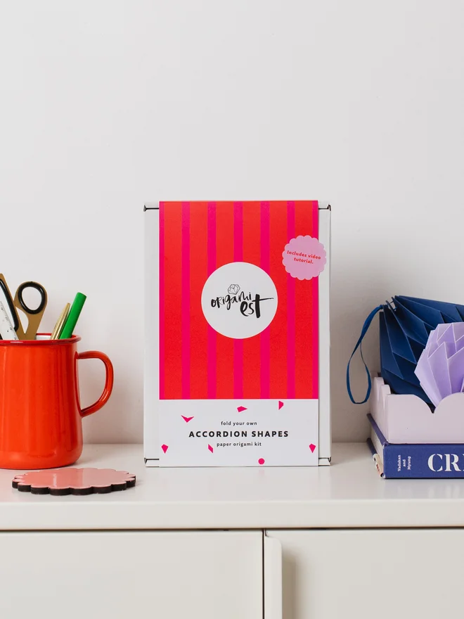 Craft kit on a cabinet surrounded by craft materials and paper ornaments.