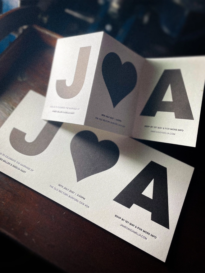 Amour Mono luxury personalised letterpress wedding invitation, shown open as a three-panel concertina with bold black initials and heart on Pristine White Colorplan card.