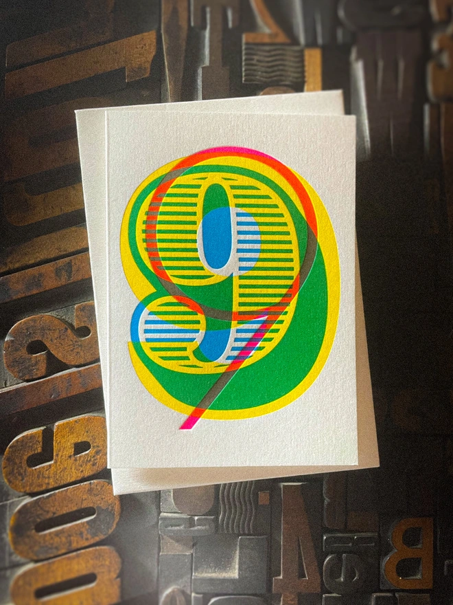 Handmade letterpress 9th birthday card featuring bold overlapping numerals printed in vibrant fluorescent cyan, magenta and yellow inks. Each card is individually hand printed using traditional letterpress techniques on luxury paper stock, creating a beautifully tactile finish with a deep impression and rich layered colours inspired by the CMYK printing process. Printed on a traditional letterpress from 1915. A wonderful artisan printed birthday card.
