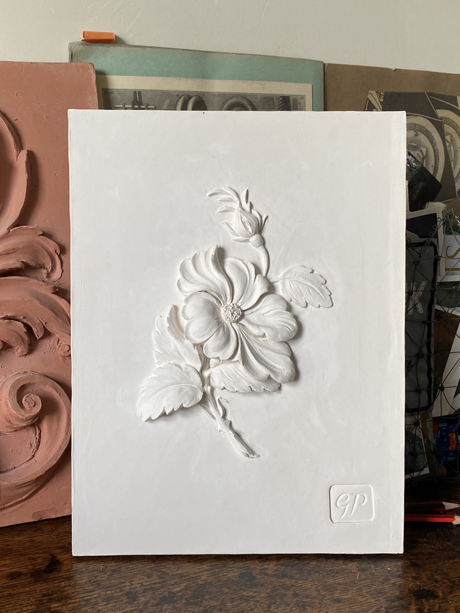 Decorative plaster wall plaque with Wild Rose design on a table with scrapbook and maquette behind
