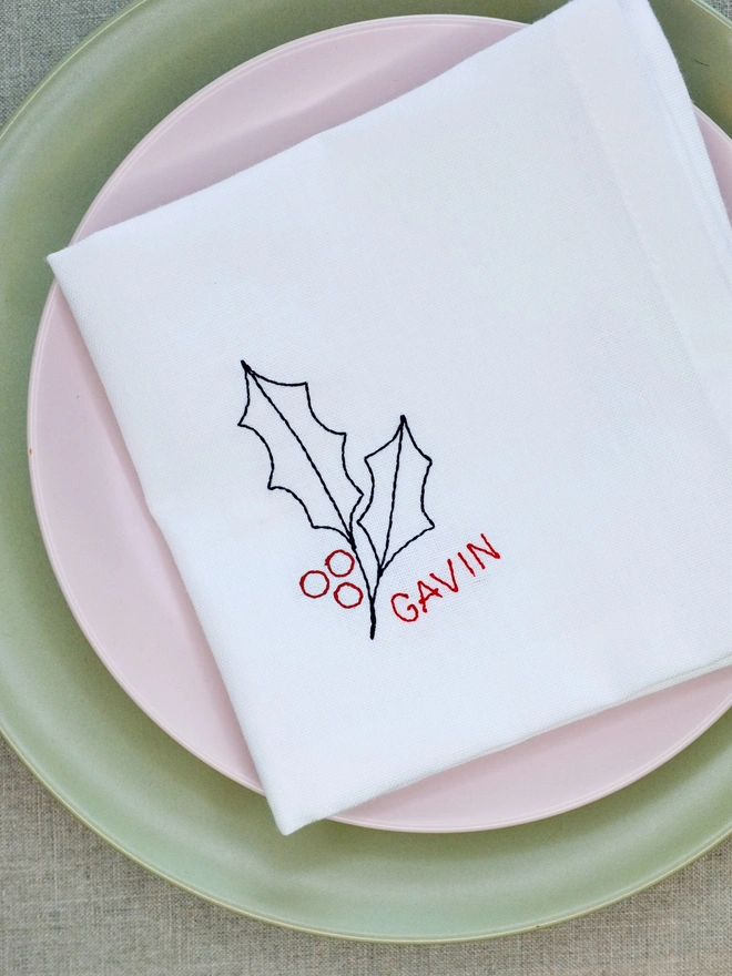 Holly embroidered napkin with custom name in red block text, cotton Christmas napkin