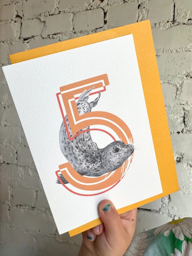 A white card featuring a big orange number 5 and a harbour seal illustration with a bright yellow envelope