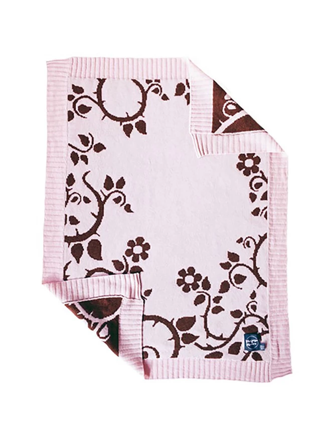 Product shot of the front of the blush briar rose baby blanket, blush pink background with a trailing design of flowers and thorns in chocolate brown.