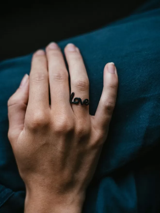 Love ring in black seen on someone's hand.