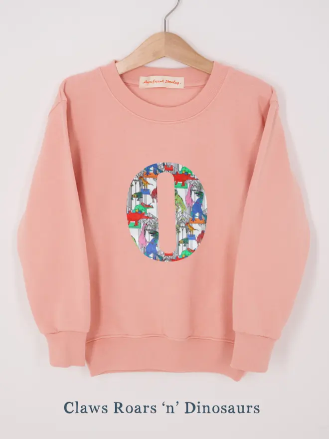 a personalised dusty pink sweatshirt with her initial sewn on the front in dinosaurs liberty print 