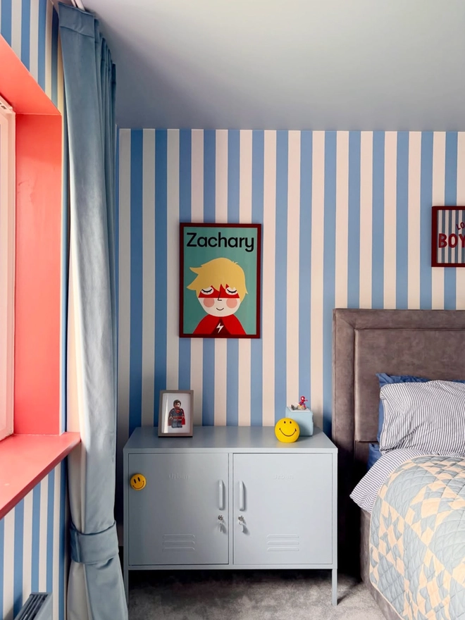 Children's bedroom with striped walls, a bed, and decorative items. A superhero portrait of a boy with the name Zachary hangs on the wall.