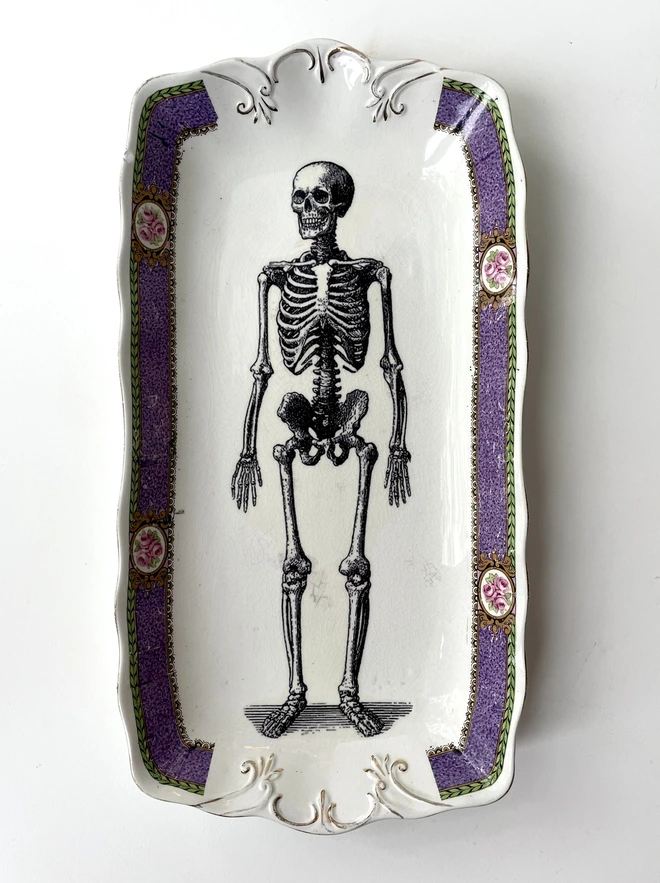 vintage plate with an ornate border, with a printed vintage illustration of a praying skeleton in the middle 