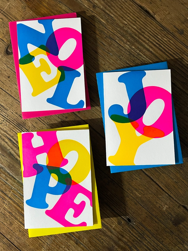 Noel, Joy, Hope; A beautiful typographic set of letterpress Christmas cards. Printed with rich vibrant and fluorescent blue, magenta and yellow inks with luxury matching and contrasting envelopes; ideal to send to your designer friends at the festive season