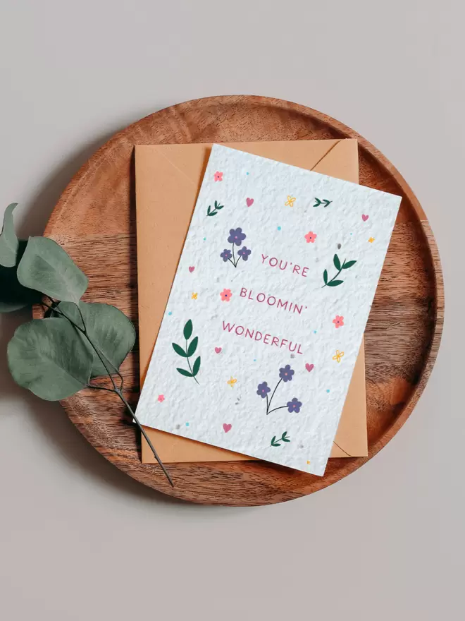 Seeded Paper Greeting Card with ‘You’re Bloomin Wonderful’ in the centre surrounded by floral illustrations on a wooden tray next to a Eucalyptus branch