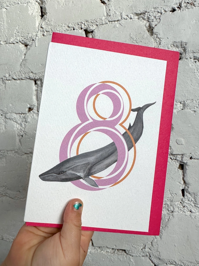 white card with a big pink number 8 and an illustration of a fin whale with a neon pink envelope