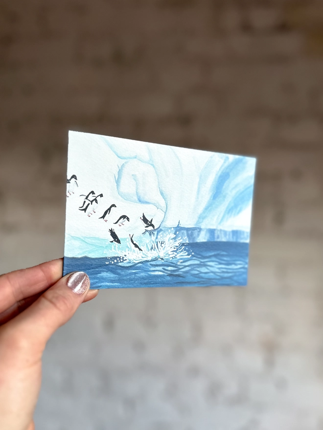  a greetings card featuring an illustration of an icy landscape with penguins diving into the sea