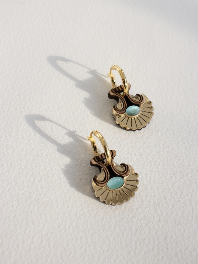 Pair of gold hoop earrings with natural stones on a light gray background