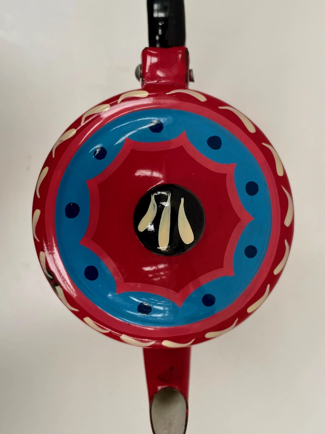 Lid of red coffee pot, featuring a blue and pink scalloped design.