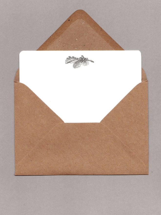 White notecard with black acorns at the top inside an open kraft envelope
