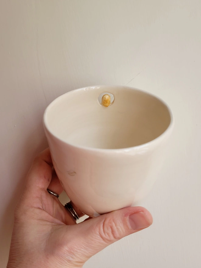 pottery drinking vessel with being held in a hand showing the inside rim with the back of a mini modelled ceramic barn owl in a cream colour