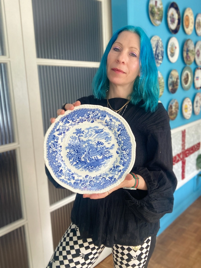A Chinese style blue and white china plate portrays three people standing near a property. One is holding a fishing rod. A Chinook helicopter flies overhead.