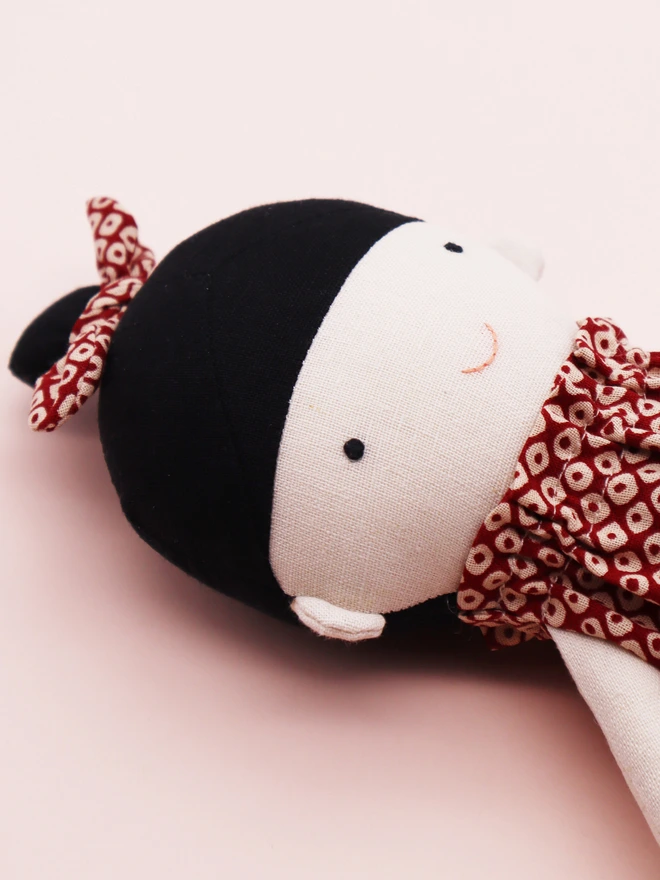 A handmade doll wearing a red and white Japanese shibori patterned jumpsuit with a matching bow in her black hair. 