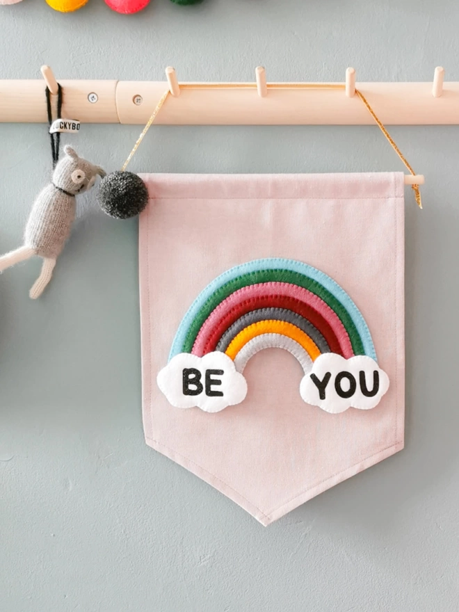 A lilac banner with a colourful rainbow with clouds with the words be you