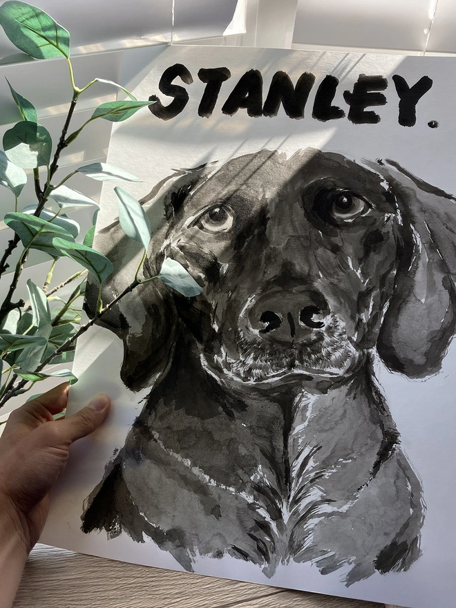 A hand holding a personalised dog portrait by artist 'Dogs by Jeff'