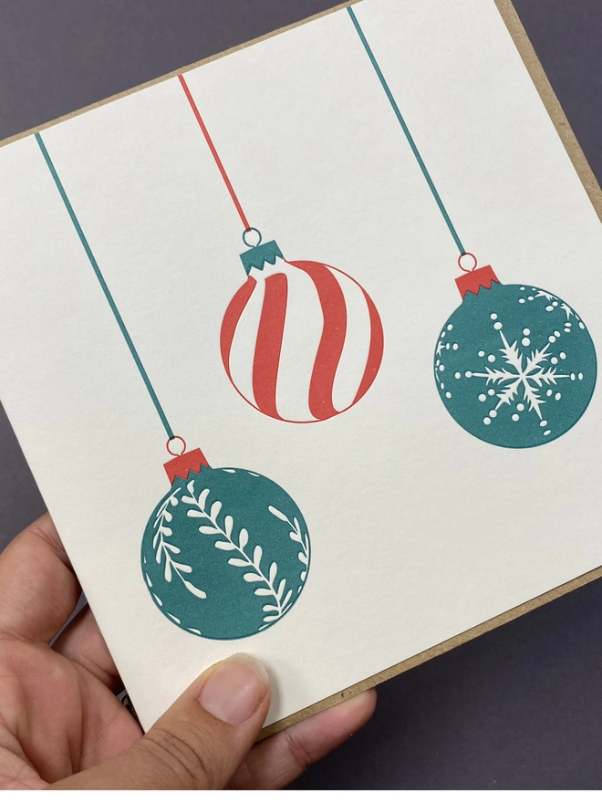 A hand holding the green and red trio bauble big card