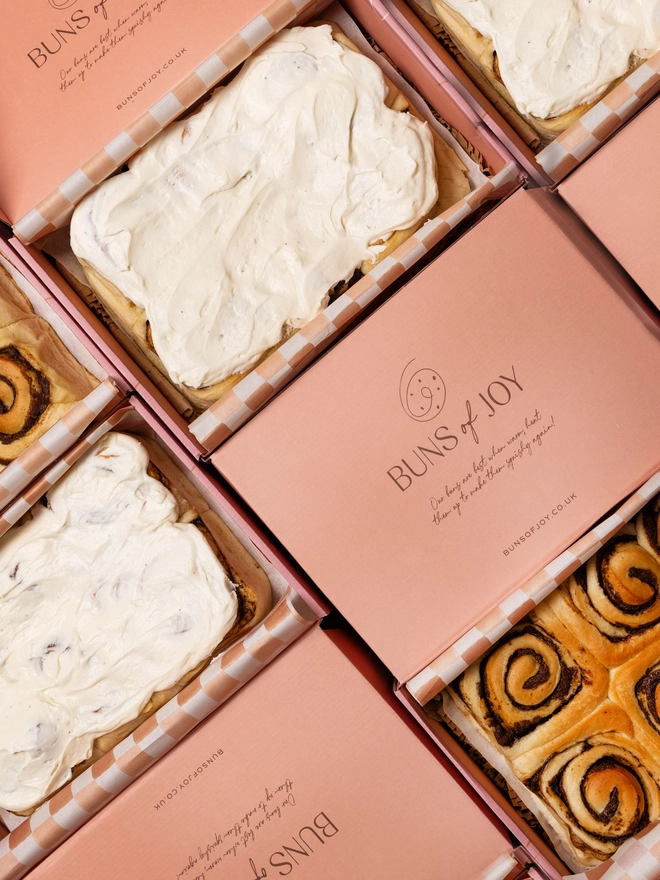 batches of cinnamon buns covered in frosting, in branded gift boxes