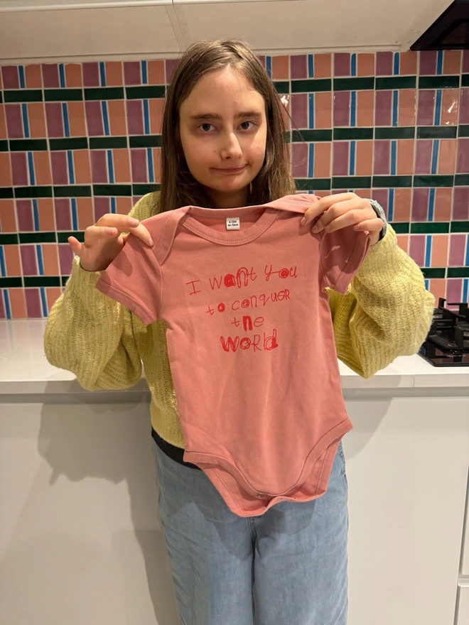 Piper holding up her design on a pink baby grow with her red font