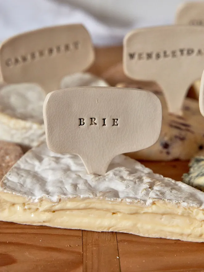Ceramic cheese marker. That reads Brie placed on a wooden tray 